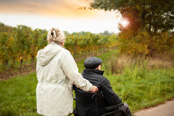 Elderly couple taking a walk outdoors in park with help of wheelchair