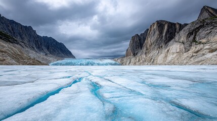 Glacier field in Alaska with deep blue ice cracks, surrounded by dramatic rocky cliffs under cloudy sky