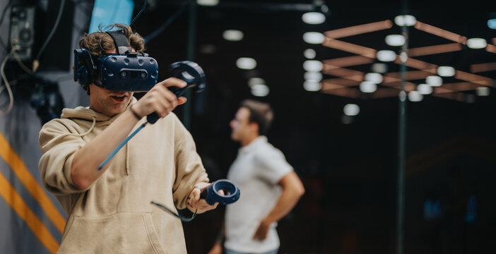 A young man fully immersed in an engaging virtual reality experience wearing VR goggles, holding controllers, with a blurred background that adds depth and a sense of movement.