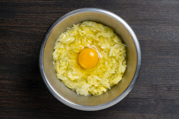 Grated zucchini with an egg in a metal bowl on a wooden table, closeup, top view. Raw materials for the preparation of vegetable waffles, pancakes. Food concept