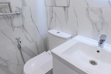A clean bathroom features white marble-patterned tiles, a white toilet, and a matching sink. The...