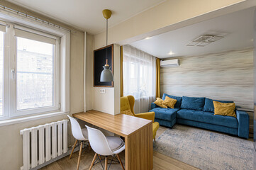 bright living space features a window, a wooden table with white chairs, a blue couch, and a yellow armchair. A modern, cozy design