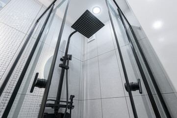 Modern shower with a black square head, framed by glass doors. Clean, tiled walls complete the minimalist look