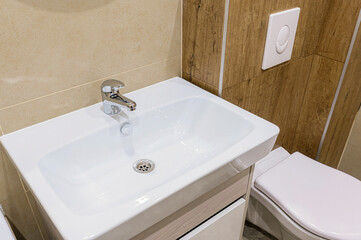 Close-up shot of a modern bathroom featuring a white sink with a chrome faucet, and a toilet. Tiled walls in neutral tones and wood paneling enhance the clean, contemporary design