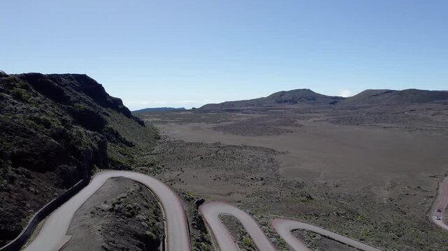 Aerial view of a car driving along a winding volcanic road in Plaine des Sables, Reunion Island. Dramatic desert-like black sand terrain and volcanic landscape.