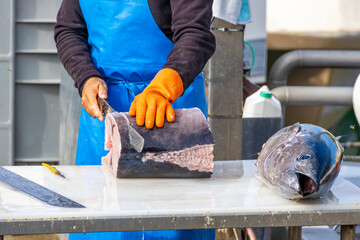 Fisherman cutting fresh tuna on table at market, close-up of fish processing, seafood preparation and traditional fishing industry scene.