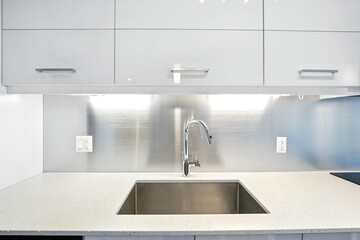 Stainless steel sink sits on a white countertop in a modern kitchen