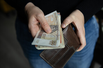 Close-up of hands holding Polish banknotes and a brown leather wallet. The person is pulling out a 200 zloty bill.