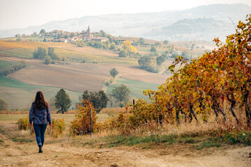 Woman walks through vineyard towards Italian village in autumn