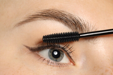 Woman applying mascara onto her eyelashes, closeup