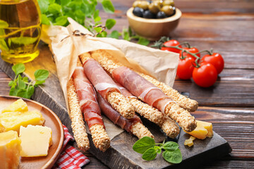 Grissini breadsticks with prosciutto, cheese, olives and tomatoes on wooden table, closeup