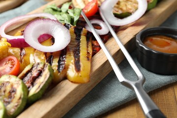 Vegetarian barbecue. Tasty grilled vegetables, sauce and carving fork on wooden table, closeup