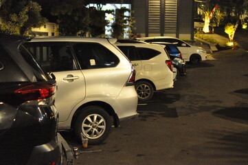 Row of parked cars in a night parking lot illuminated by lights, showing urban transportation, modern vehicles, and outdoor city lifestyle.
