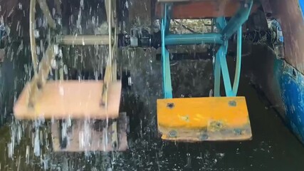 Rotating catamaran paddles in water, showcasing mechanical movement and splashes. Wooden and metal paddle wheels powered by pedal drive, propulsion system. Energy production.