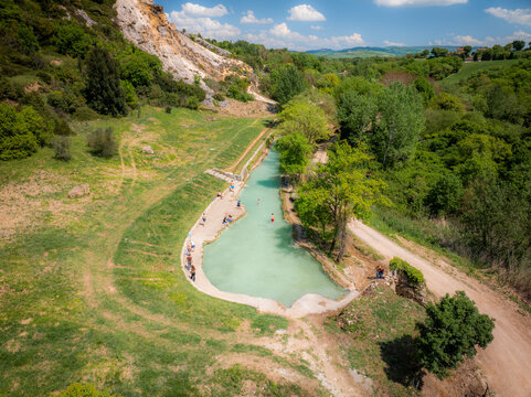 Aerial view of thermal waters cascading into turquoise pools, nestled amidst verdant hills and rugged cliffs, a serene oasis under the Tuscan sun, Bagno Vignoni, Tuscany, Italy.