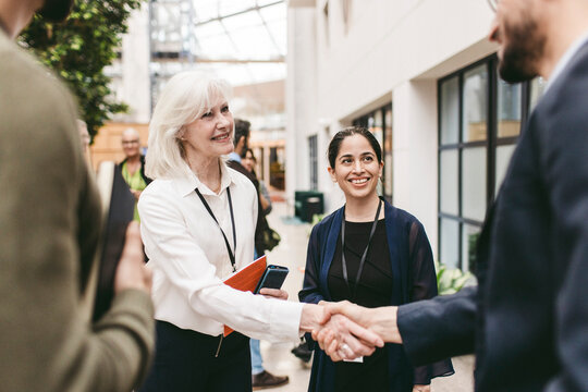 Smiling senior female business expert shaking hand with male colleague at networking event in convention center