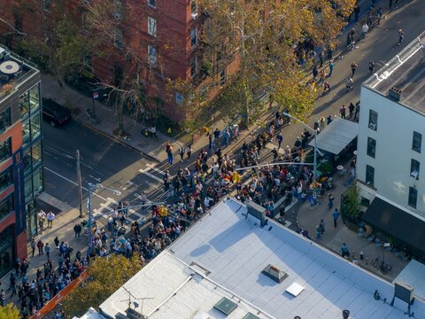 Aerial view of crowds gathering at an intersection near brick buildings cheering on Marathon runners, bathed in the warm afternoon light, Brooklyn, New York, United States.