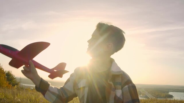 Scene features boy in plaid shirt racing with red glider during sunset, view follows dynamic action as camera tracks his movement beside sparkling landscape. Slow motion. Portrait.