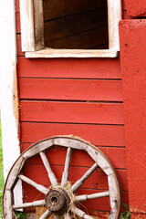 A wagon wheel sits on the window of a red barn