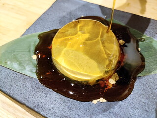 黒い石皿の上に笹の葉を敷きその上に水ゼリー餅が置かれ上から黒蜜がかけられている様子を捉えた和風のデザートの写真です。和の涼しげな雰囲気が漂います。 © BRUCE