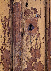 Close-up of a weathered wooden door with peeling paint and a keyhole.