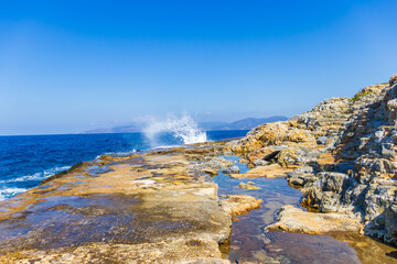 Waves near the rocky shore. The sea with crashing waves on the rocks and the stone shore against the blue sky.