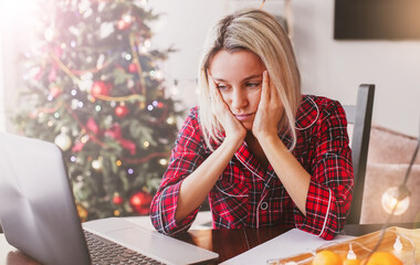 Sad middle aged woman working at the home office by laptop during Christmas holiday