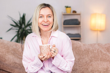 Adult woman sitting on the sofa at home and having a cup of coffee