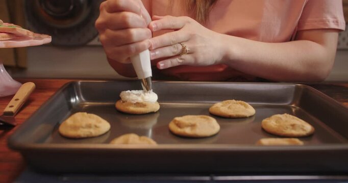 Piping frosting onto baked cookies on a baking sheet