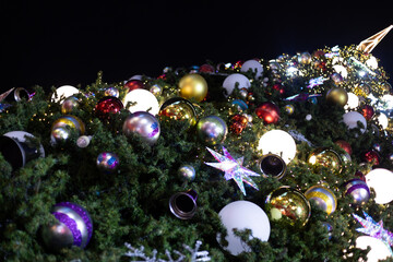 close up multicolor decoration ball with snow star and light bulb on Christmas tree pile tree at night time on holiday snowy xmas theme in december 