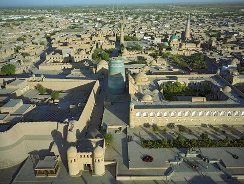 Aerial view of ancient city walls casting stark shadows, contrasting with the sun-drenched buildings and minarets, Khiva, Uzbekistan.