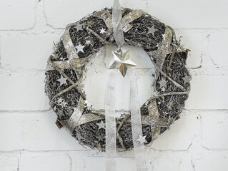 A modern silver Christmas wreath with stars on a white brick wall.
