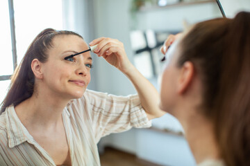 Woman applying mascara in front of mirror