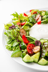 Fresh vegetable salad with cherry tomatoes, cucumbers, bell peppers, olives, leafy greens, and creamy cheese on a white plate. Healthy, colorful, and appetizing food presentation.