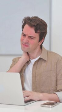 Vertical Video, Young Man having Neck Pain while Working on Laptop