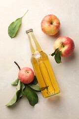 Delicious cider in glass bottle and apples with green leaves on beige table, flat lay
