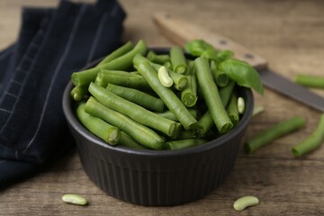 Pieces of fresh green beans in bowl on wooden table, closeup