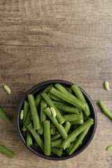 Pieces of fresh green beans in bowl on wooden table, top view. Space for text