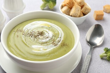 Tasty broccoli cream soup served with croutons on light grey table, closeup