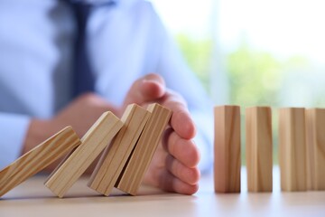Risk. Man stopping domino effect at table, closeup