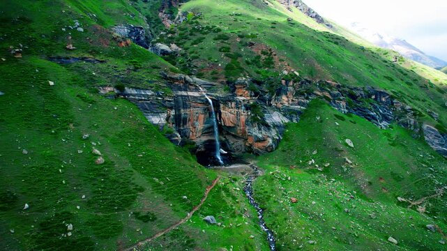 4K Aerial shot of beautiful waterfall in mountain valley during summer season at Sural Bhatori, Pangi Valley, India. Para Lam waterfall flowing from cliff, surrounded by green grass. Nature background