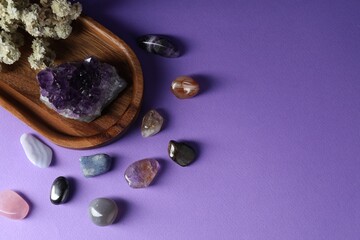 Different beautiful gemstones and flowers on purple background, flat lay. Space for text