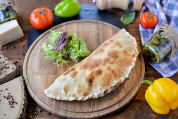 
Calzone on a wooden round board with salad on the table