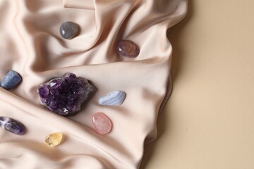 Different beautiful gemstones and cloth on beige background, top view. Space for text