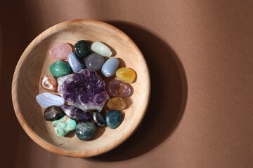 Different beautiful gemstones in bowl on brown background, top view. Space for text