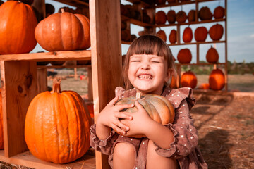 Happy little beautiful child girl hugging a ripe pumpkin with her arms. Market trading and fair of...