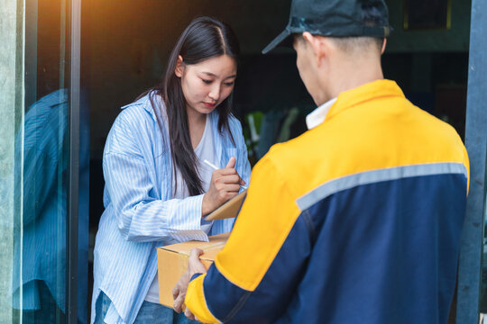 Young Woman Receives Package at Doorstep from Delivery Person in Casual Clothing During Daylight in Urban Environment