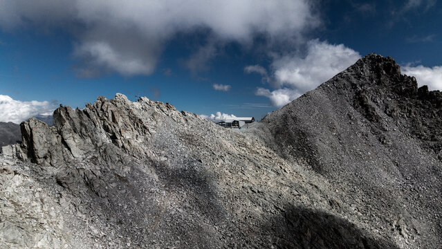 Aerial view of rugged, sun-kissed mountain peaks piercing the sky, shadowed slopes contrasting with the bright, rocky terrain, Brescia, BS, Italia.