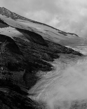 Aerial view of the contrasting textures of snow-capped mountains meeting the rugged terrain below under a dramatic, cloudy sky, Brescia, BS, Italia.