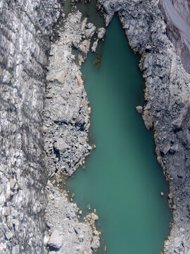 Aerial view of a serene, turquoise lake nestled between rugged, rocky cliffs, a stark contrast of smooth water and rough stone, Brescia, BS, Italia.